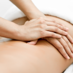Mãos de massoterapeuta pressionando suavemente as costas de um cliente, em um ambiente de massagem terapêutica.