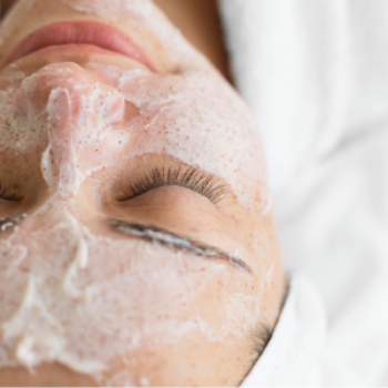 Rosto de pessoa com olhos fechados coberto por espuma branca de limpeza facial, sugerindo um tratamento de pele relaxante.